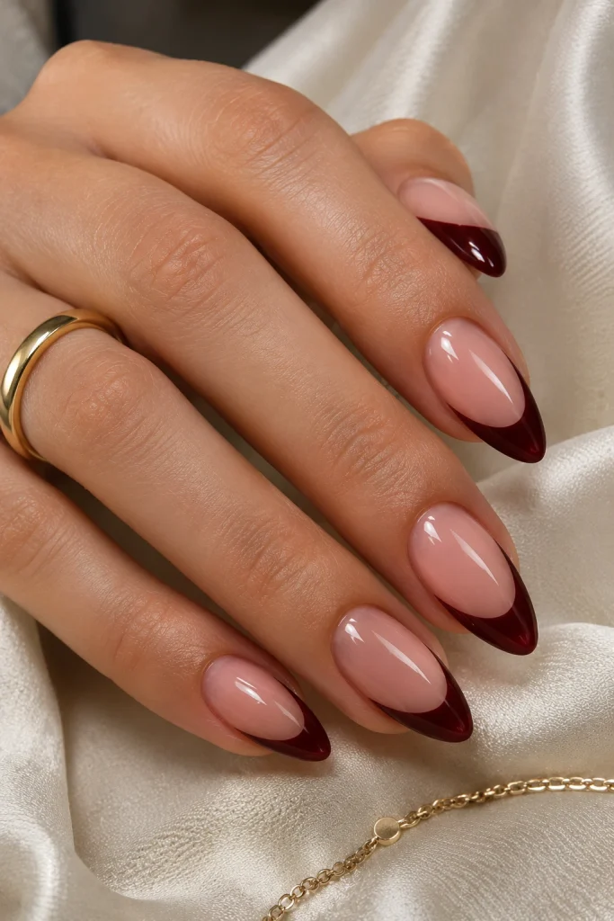Almond nails with sheer nude bases and deep cherry cola French tips.