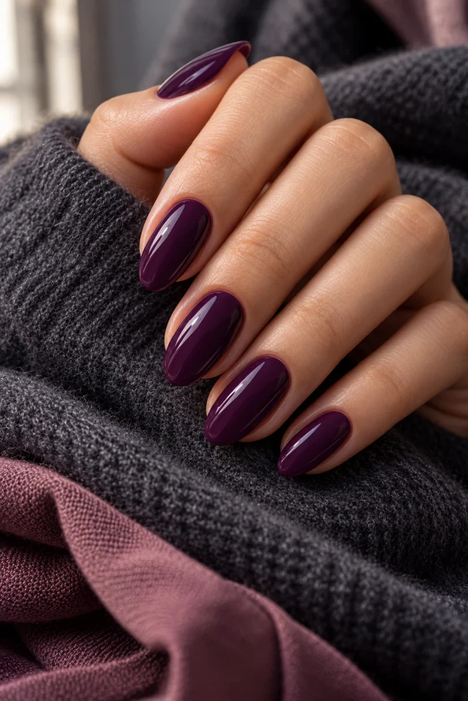 Deep dark plum polish on medium almond nails with a smooth glossy finish.