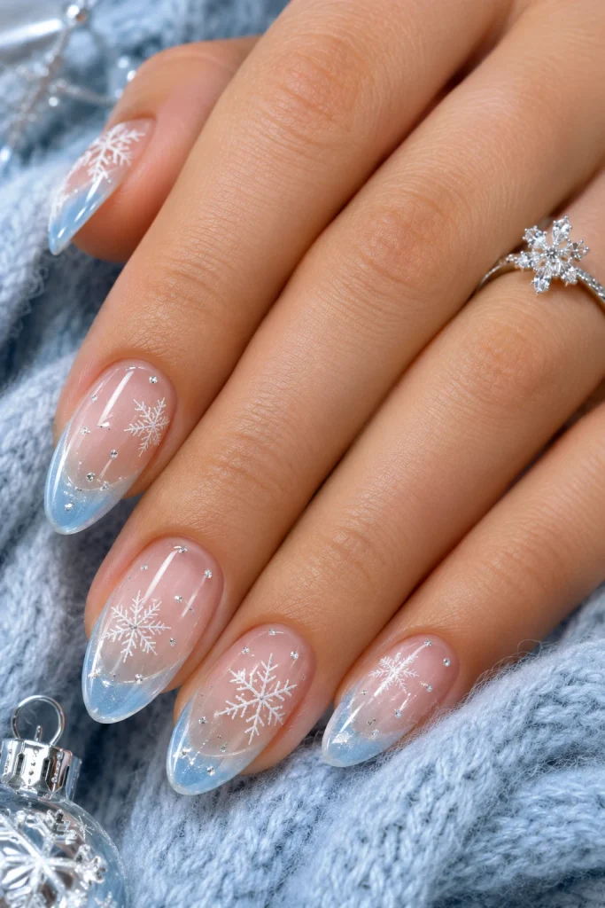 Icy blue French tip nails with tiny white snowflakes and silver snow-like dots.
