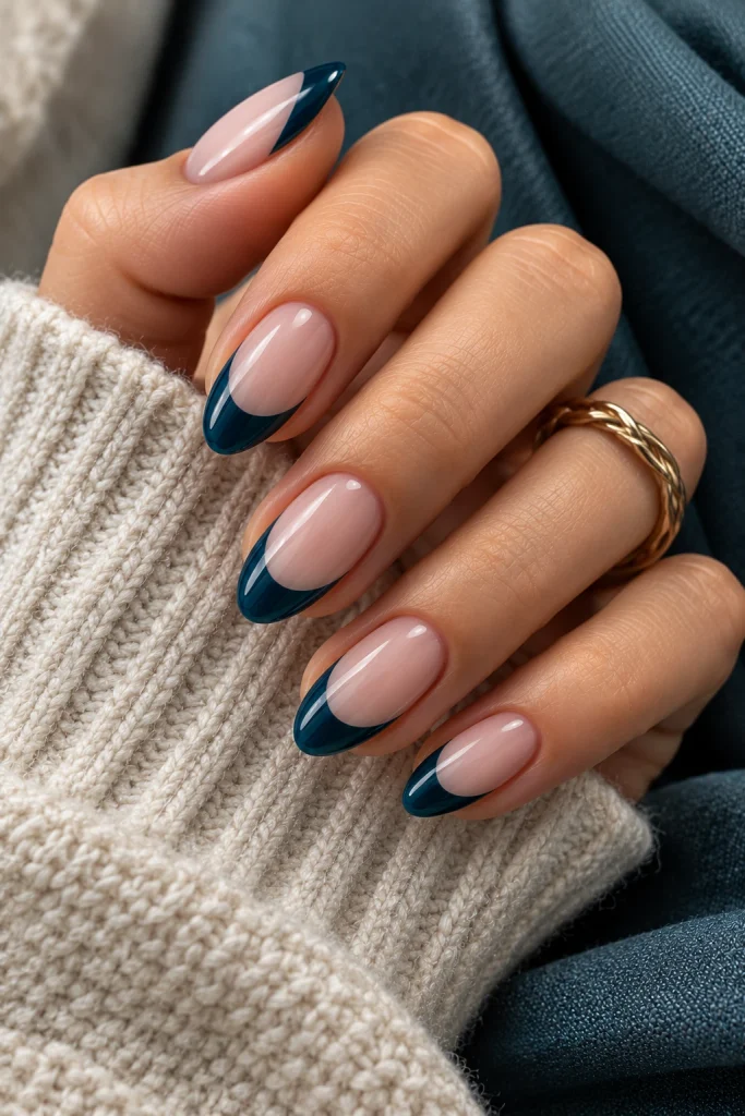 Sheer nude almond nails with deep petrol blue French tips.