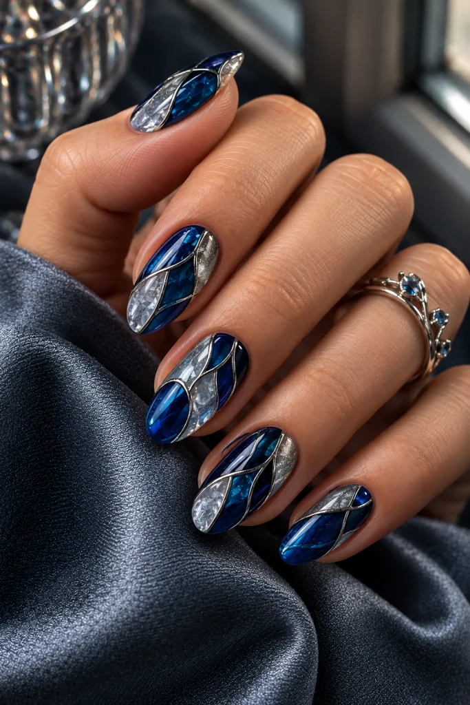 Alt text: Sapphire blue and icy silver stained glass nail design with translucent panels and fine metallic outlines.